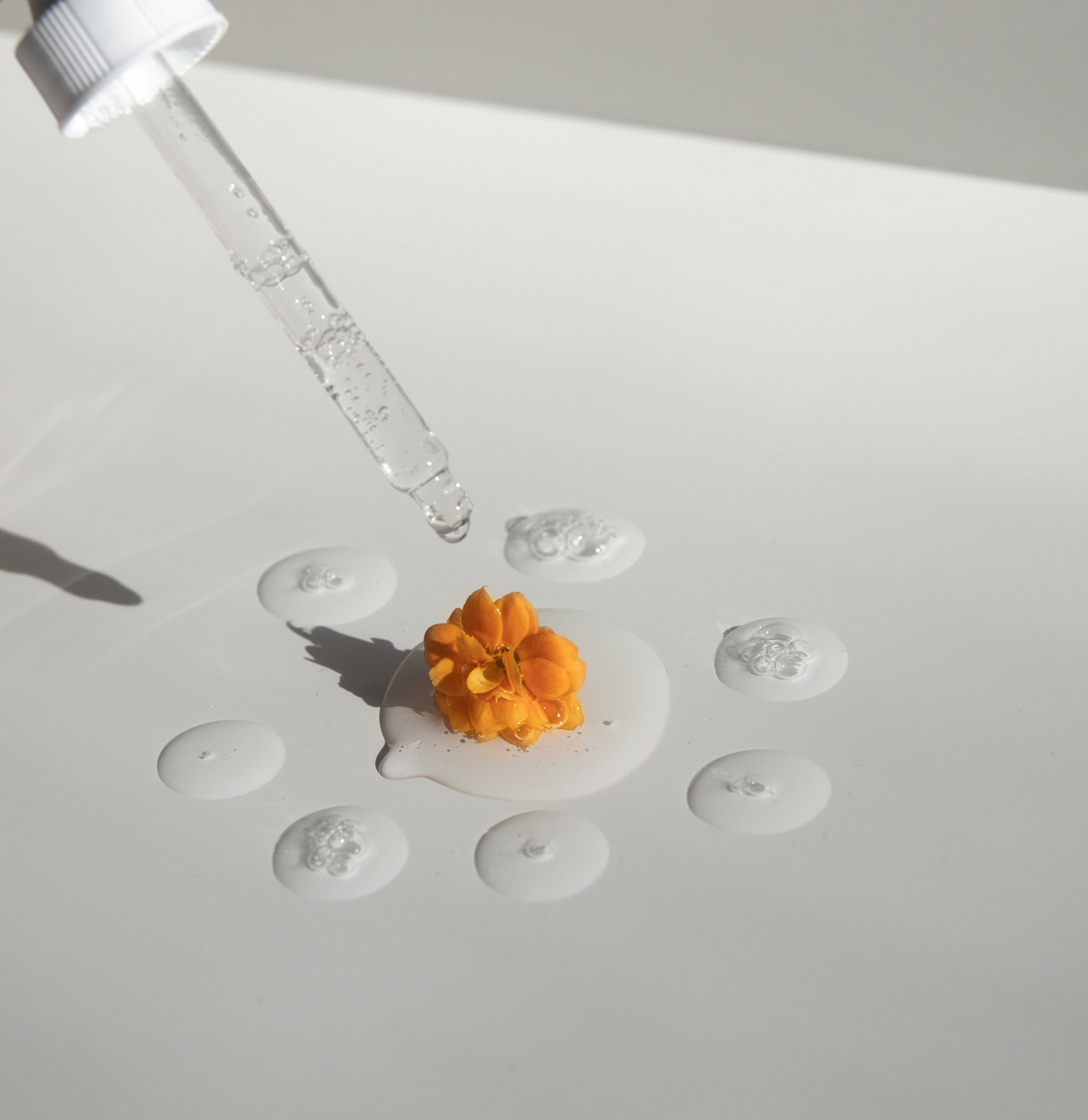 Pipette mit tropft durchsichtige Flüssigkeit auf den Tisch mit orangener Blüte